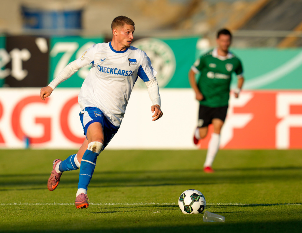 Michael Cuisance (Hertha BSC, #10) am Ball, waehrend ein Becher aus den Zuschauerrangen auf dem Spielfeld liegt.