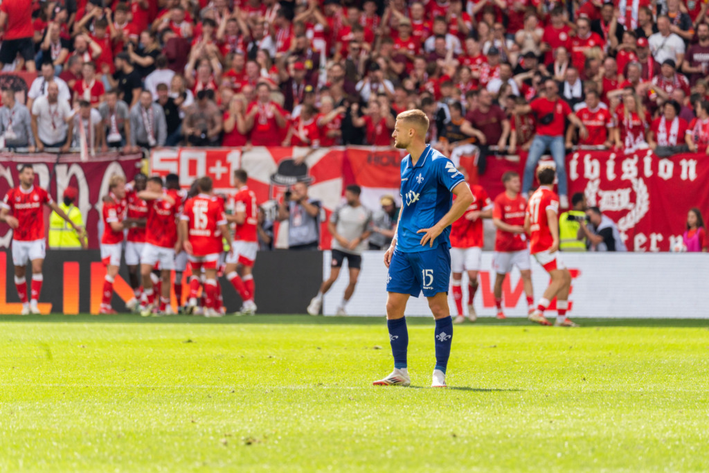 1. FC Kaiserslautern vs. SV Darmstadt98: Fabian Nürnberger enttäuscht im Vordergrund, jubelnde Lauterer im Hintergrund.